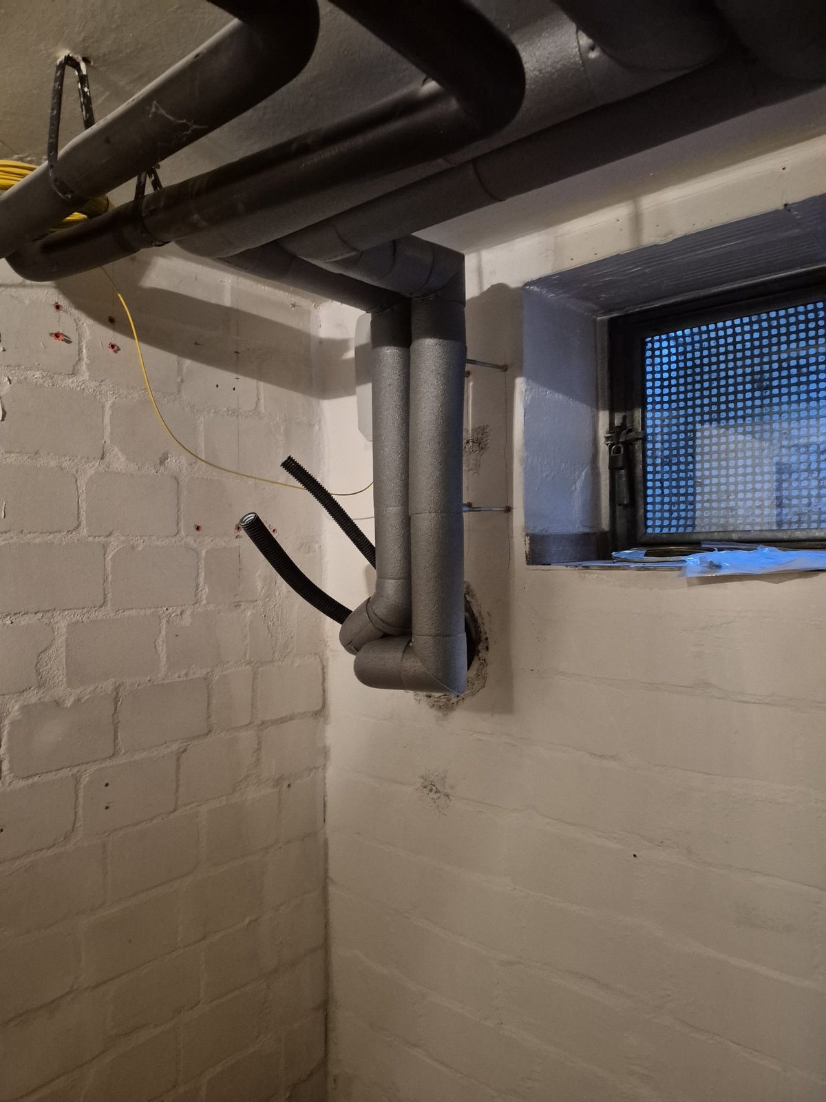 Gedämmte Rohrleitung und Leerrohre an der Wanddurchführung im Keller